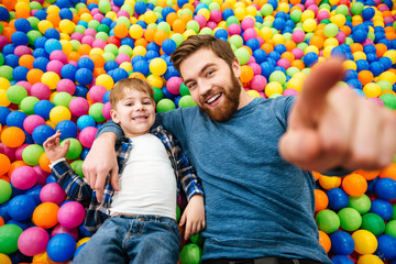 Fototapeta na wymiar Boy and his father playing at pool with colorful balls