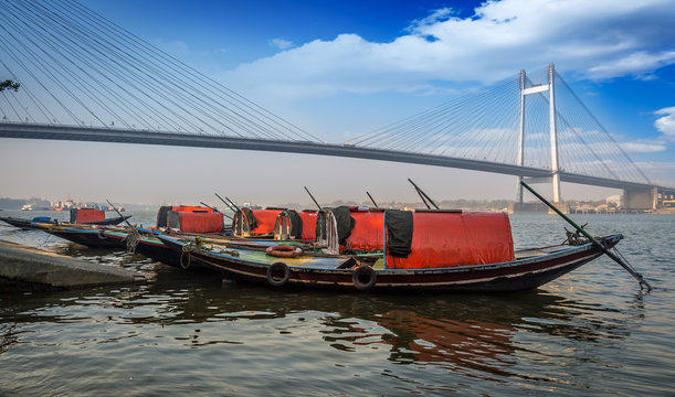 Wooden boats lined up at the Hooghly river bank overlooking the famous Vidyasagar setu bridge. 