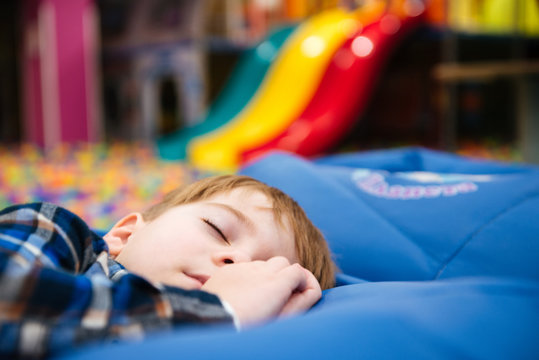 Tired exhausted little boy sleeping at indoor amusement park