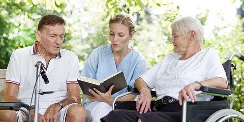 Carer reads a book to the elderly persons