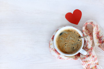 favorite beverage warms/ hot coffee in a mug wrapped a scarf, and a heart symbol, top view 
