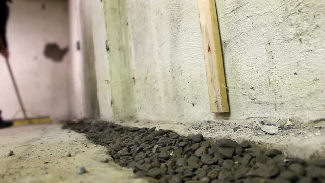 Contractor sweeps unfinished basement floor near interior french drain
