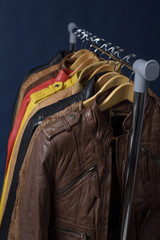 Fototapeta na wymiar Many colored leather jacket hanging on rack on blue background