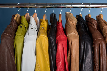 Different color leather jacket hanging on rack on blue background