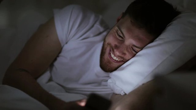 young man with smartphone in bed at night