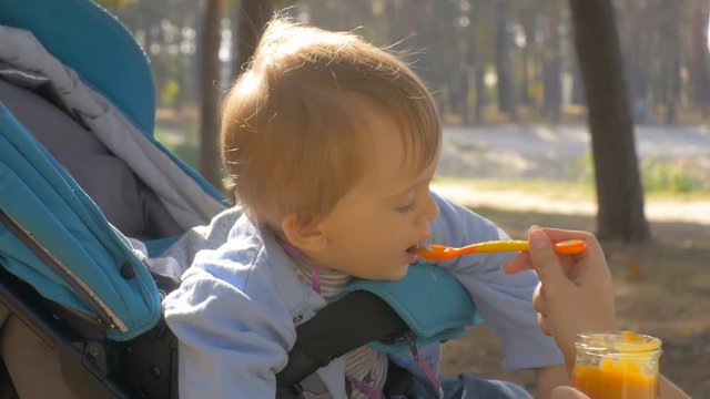 4K closeup footage of adorable baby boy sitting in pram at park and eating apple sauce from spoon