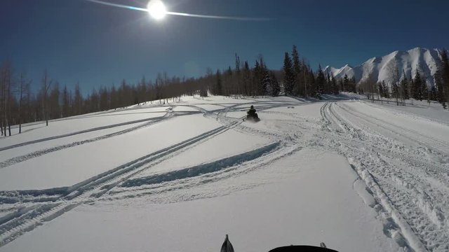 Snowmobile ride mountain peak into the sun POV. Snowmobile trail ride across high mountain meadow and forest in winter. Recreation and fun. Exciting dangerous adventure. Sport recreation.