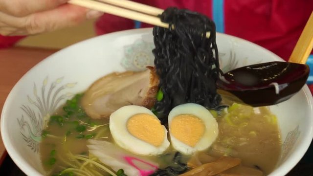 Hand eating hot Japanese ramen, black noodle with boiled egg in flavorful soup