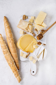 Cheese plate. Assortment of cheese with walnuts, honey and bread on white wood serving board over white concrete texture background. Top view with space.