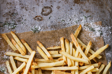 Fast food french fries potatoes with skin served with salt and herbs on baking paper over old rusty...