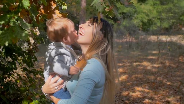 Closeup slow motion footage of happy mother hugging her baby son at autumn park