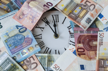 Fuenf Minuten vor zwoelf Uhr / Euro Geldscheine und eine Uhr, die Zeiger stehen fuenf Minuten vor zwoelf.