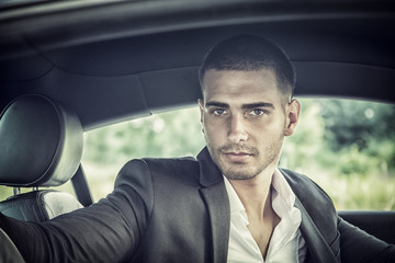 Handsome Young Man Driving a Car, wearing black jacket, hand on wheel