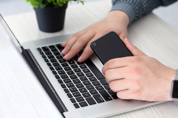 man holding phone and typing on laptop notebook keyboard