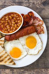 Traditional full English breakfast with fried eggs, sausages, beans, mushrooms, grilled tomatoes and bacon on wooden background
