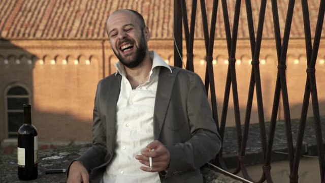 caucasian, bald  man alone laughs uproariously drinking wine