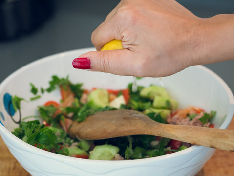 Hand squeezing lemon juice into a bowl of tuna salad.