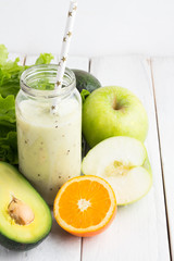 smoothie in a bottle with a straw, avocado, apple and orange on a white background