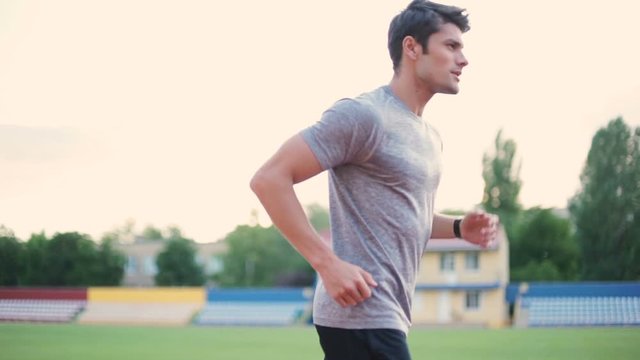 Young concentrated fitness man running on athletics running track on stadium