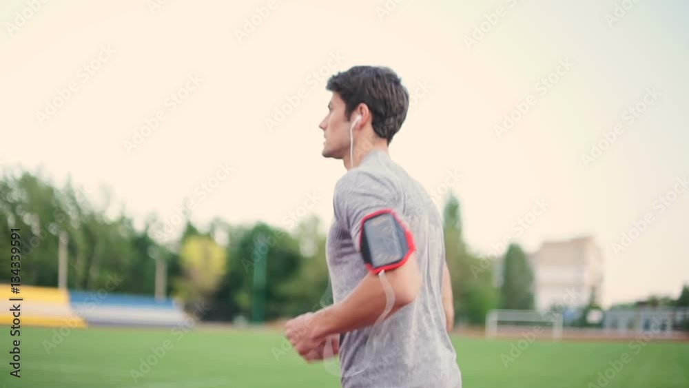 Poster young handsome sports man running down stadium track with earphones