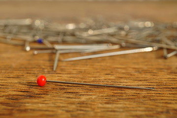 Pin with a red top separated from a heap of many silver pins used in clothing (garment) industry on the wooden background as a symbol of handmade sewing, 
fashion and manufacturing 