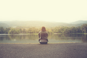 Fototapeta na wymiar Lonely women wear black jacket sit on reservoir in holiday morning.