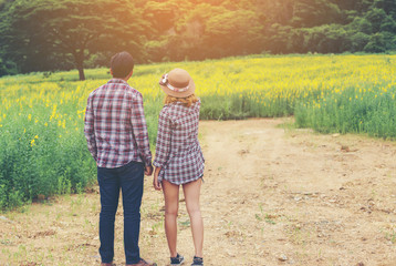 Young hipster couple relaxing in yellow flower field at summer.