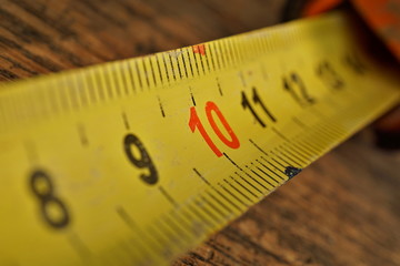 
Macro detail of yellow metal tape meter with red and black numbers measuring length in centimeters and meters on the wooden background 