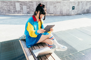 young beautiful asian millennial woman nonconformist outdoor in the city holding a tablet looking...