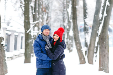 Fototapeta na wymiar portrait of pretty young happy couple in love walking and playing in winter park in red hat and pullover. happy family Valentine's Day together.