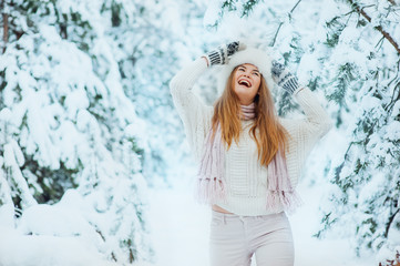 Beautiful young girl posing in the winter in cold snowy forest with pine trees.