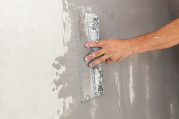 Closeup of repairman hand plastering a wall with putty knife or spatula