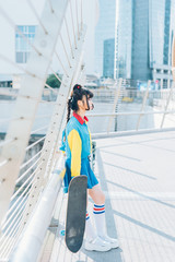 young beautiful asian millennial woman nonconformist skater posing outdoor in the city holding...