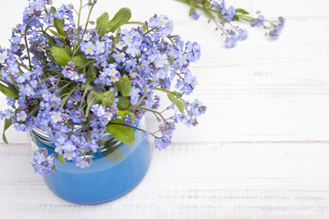 small blue flowers in a jar on a white wooden background