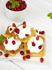 waffles with wild strawberries and whipped cream on white table