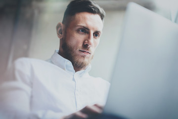 Attractice bearded businessman working in modern office.Man using contemporary notebook.Blurred background. Horizontal, film effect.