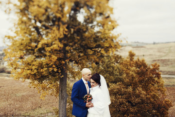 Wedding couple enjoys moment of peace standing before autumn tre