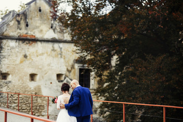 Obraz na płótnie Canvas Look from behind at wedding couple walking along bridge to the c