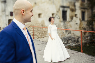 Fototapeta premium Groom looks far away posing with bride on bridge