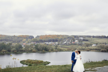 Fototapeta na wymiar Beautiful wedding couple stands before the lake in a cloudy day