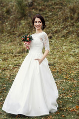 Fototapeta na wymiar Stylish bride stands with wedding bouquet on autumn ground
