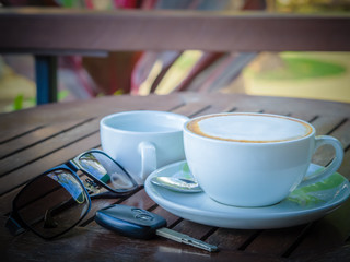 Hot coffee latte in a glass of white paste on a wooden table, With sunglasses and car keys. Travel concept.