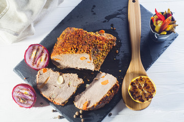 Roast pork with with mustard, onions. pepper and lemon on a white wooden table, top view. Baked meat on a black slate board, flat lay.