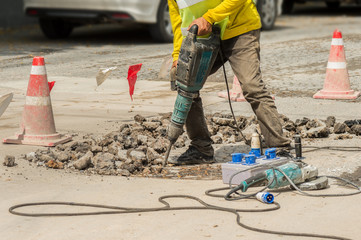 Worker drilling concrete driveway with jackhammer.
Man repairing road surface with heavy duty machine.
