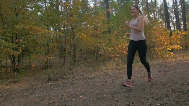 Slow motion of beautiful smiling young woman jogging in forest at evening