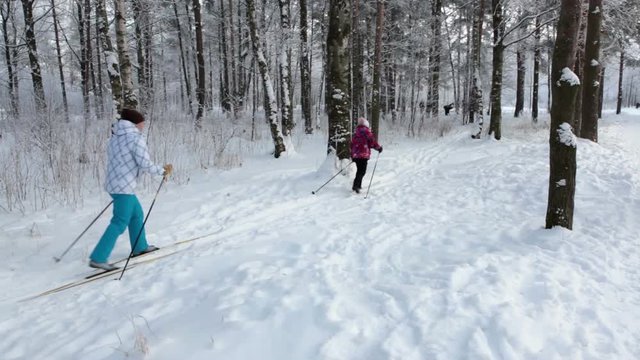 Eight years old daughter and her adult mother running on cross-country skis in winter snowy park, Russia
