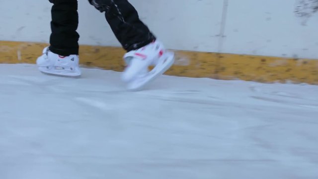 Children legs in white plastic hockey running on the ice of skate rink, camera moving
