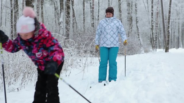 Young daughter and her mother running on cross-country skis in winter park, Russia
