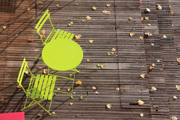 Table ronde et chaises vertes sur terrasse en teck en automne
