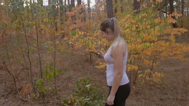 4K footage of beautiful young woman selecting music track on smartphone while running at forest